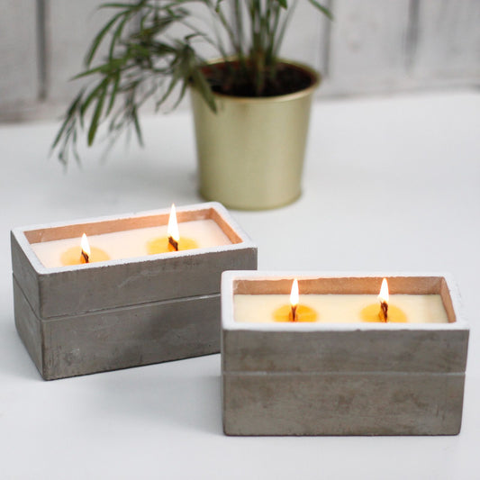 Two rectangular concrete candle holders with lit white wax candles on a white surface.