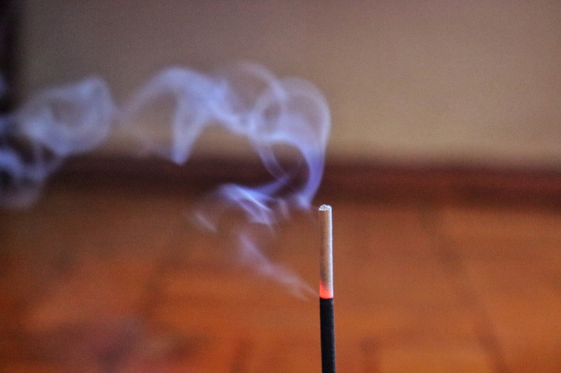 Incense stick burning, releasing wisps of smoke.
