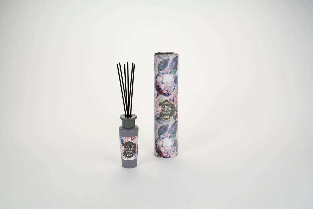 A reed diffuser bottle with black sticks beside a floral patterned cardboard tube