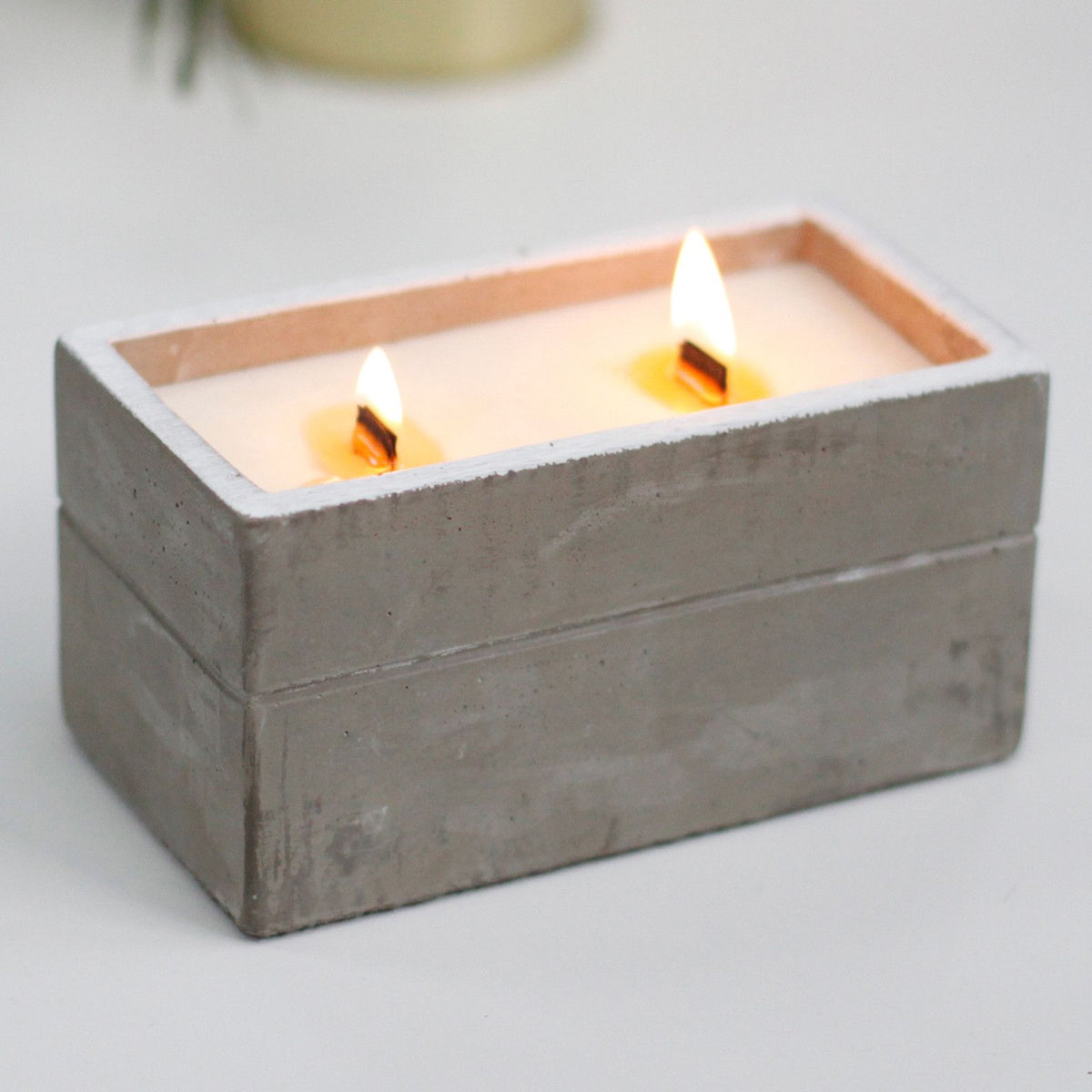 Two lit wooden wick candles in a rectangular gray concrete holder