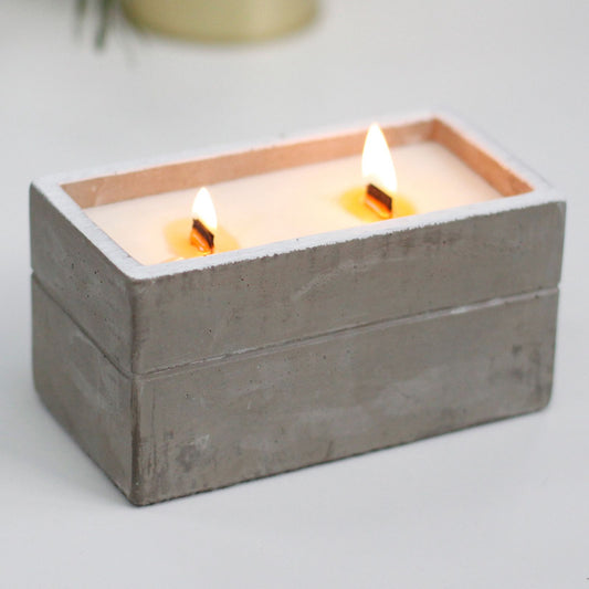 Two lit wooden wick candles in a rectangular gray concrete holder