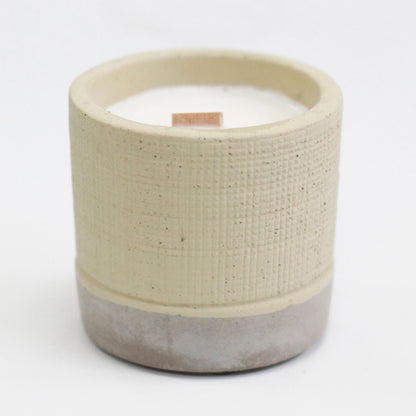 Handcrafted ceramic candle with a wooden wick and textured beige and grey finish.