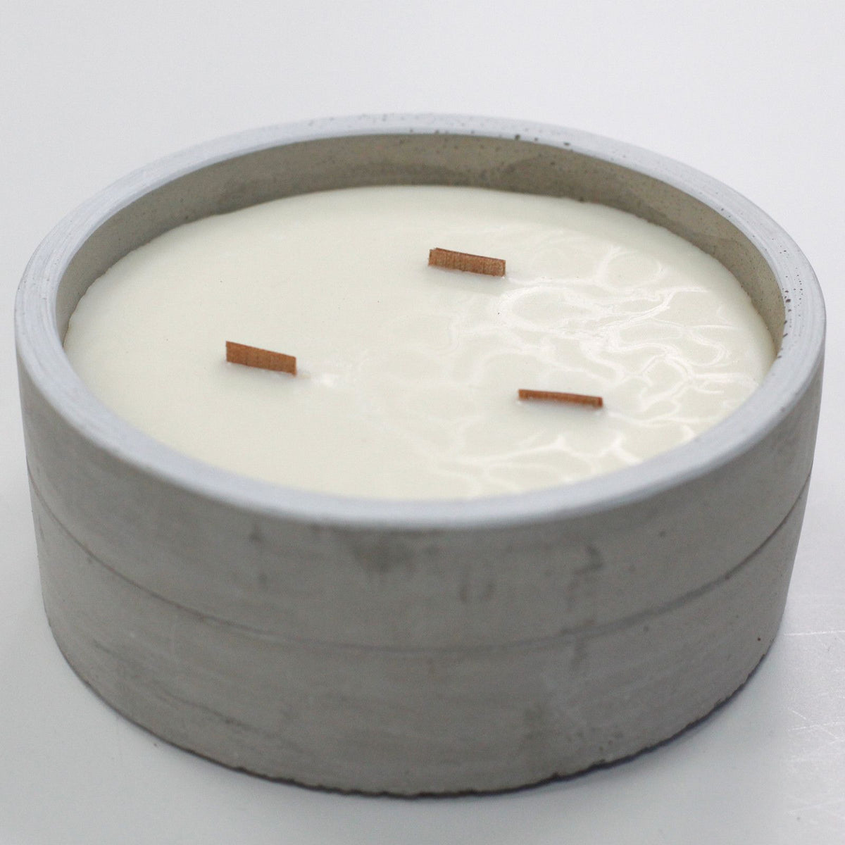 White soy candle with three wooden wicks in a minimalist grey concrete container