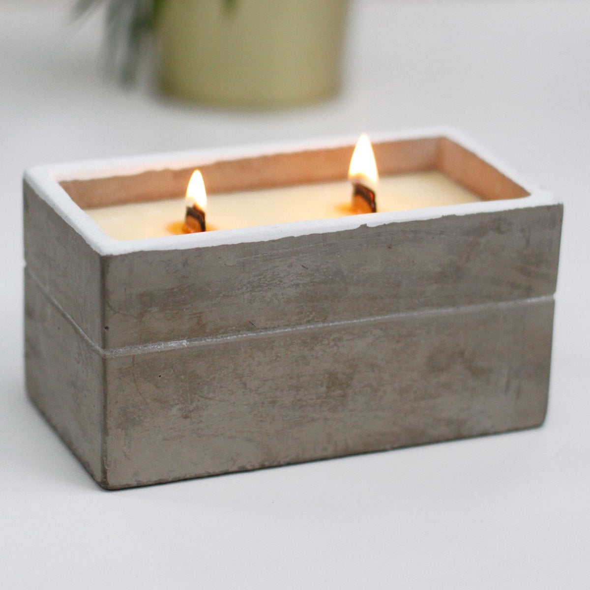 Two-wick scented candle in a rectangular grey concrete container with wooden wicks lit