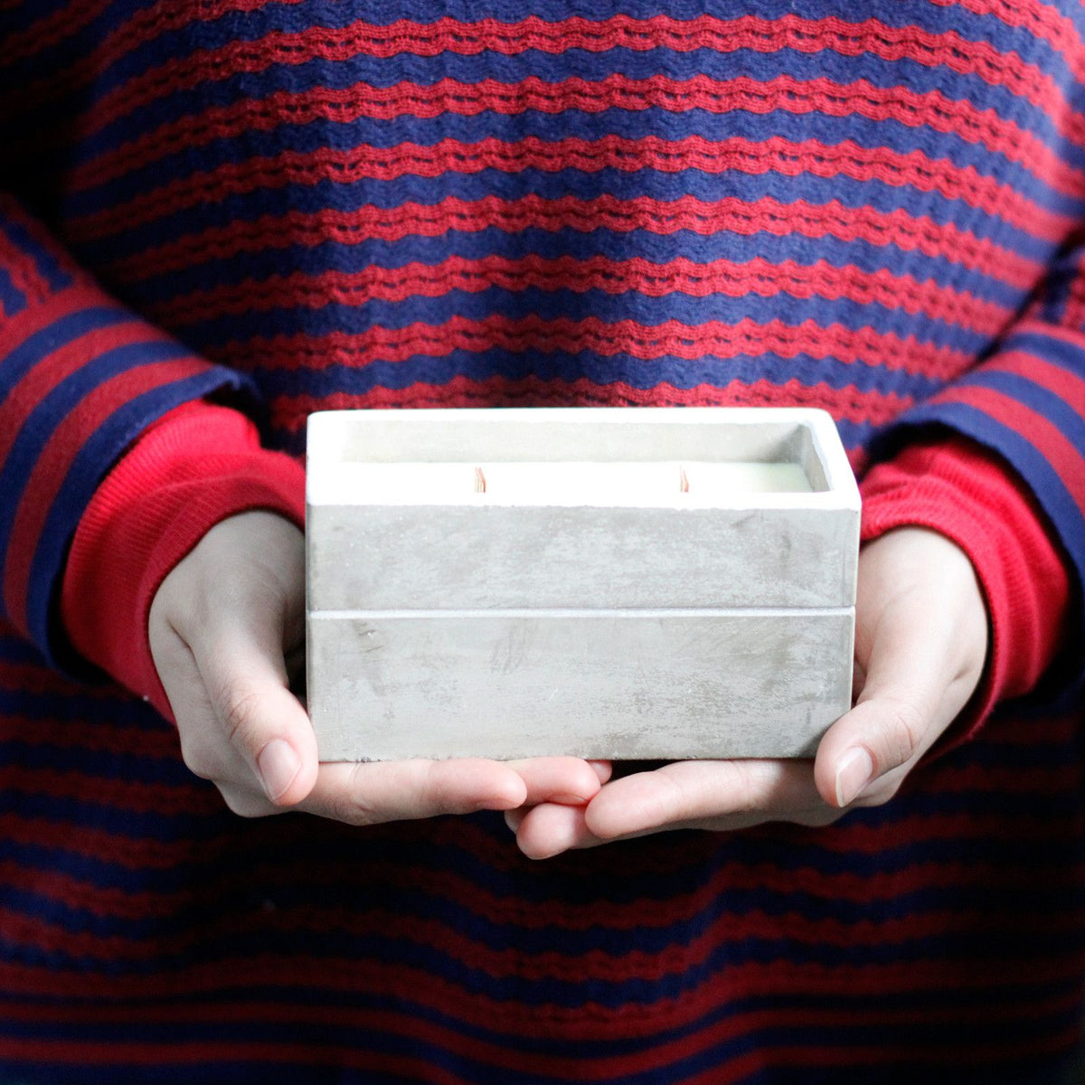 Hands holding a rectangular white concrete candle holder