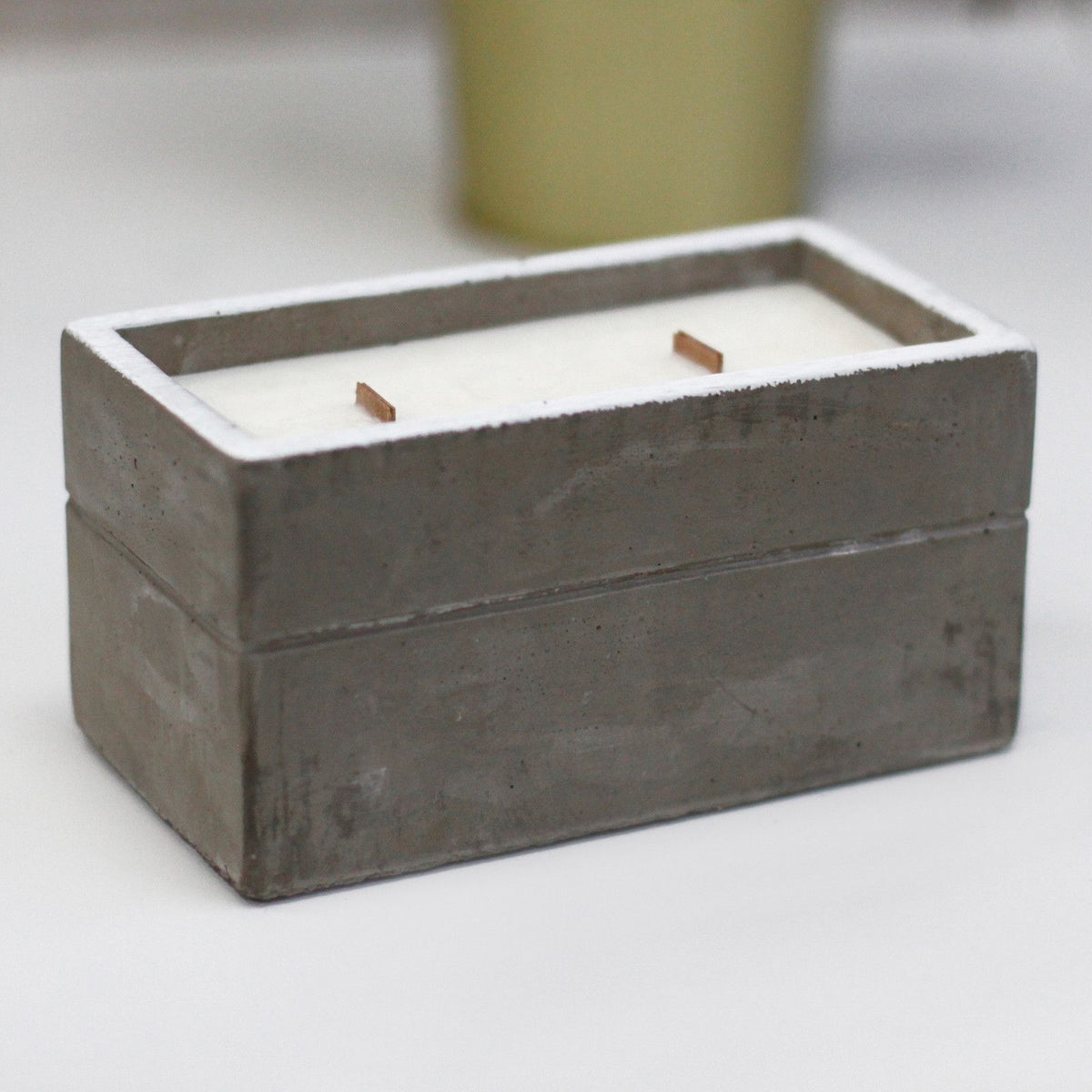 Rectangular grey concrete candle holder with white wax and two wooden wicks.