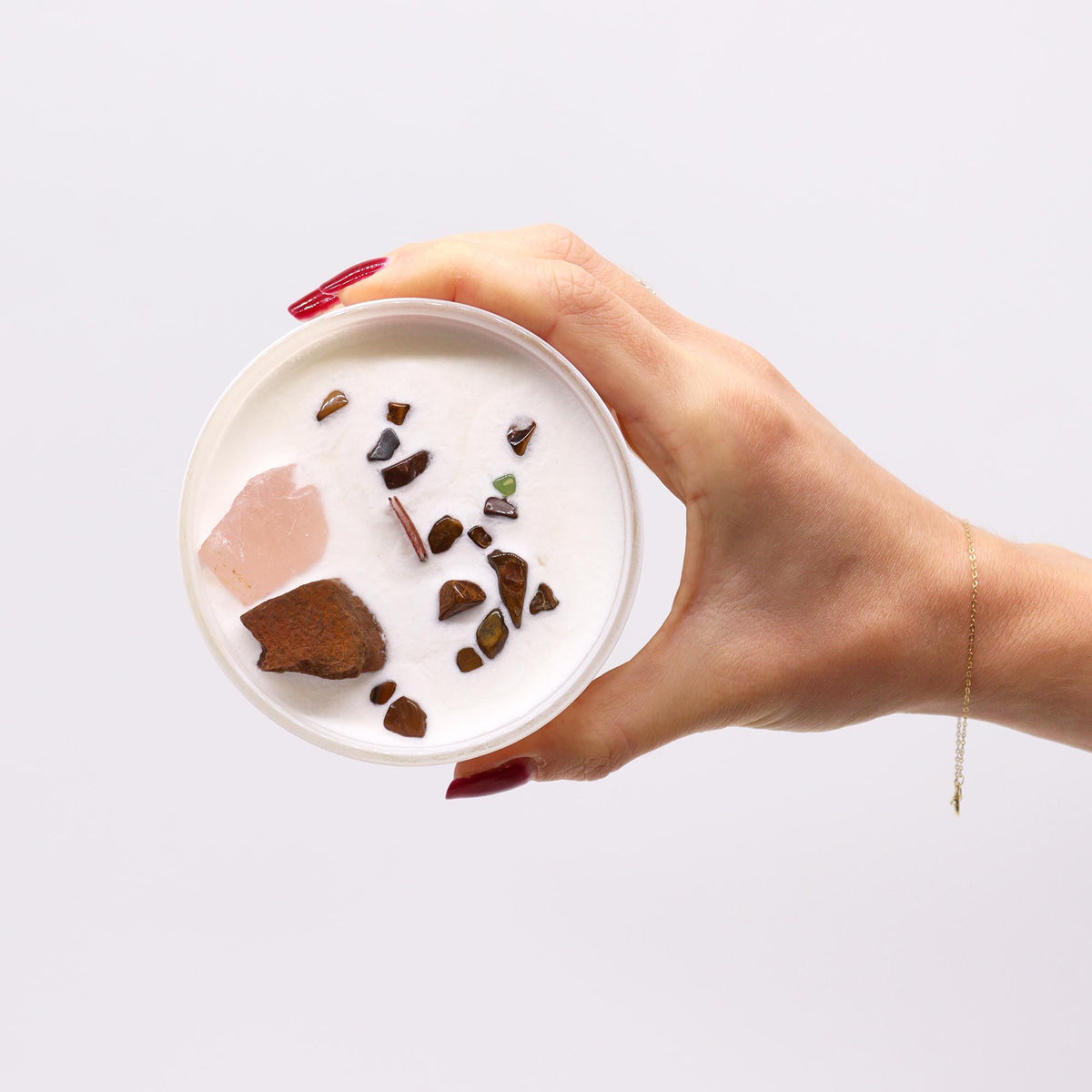 Hand holding a white scented candle topped with various natural crystals and gemstones.