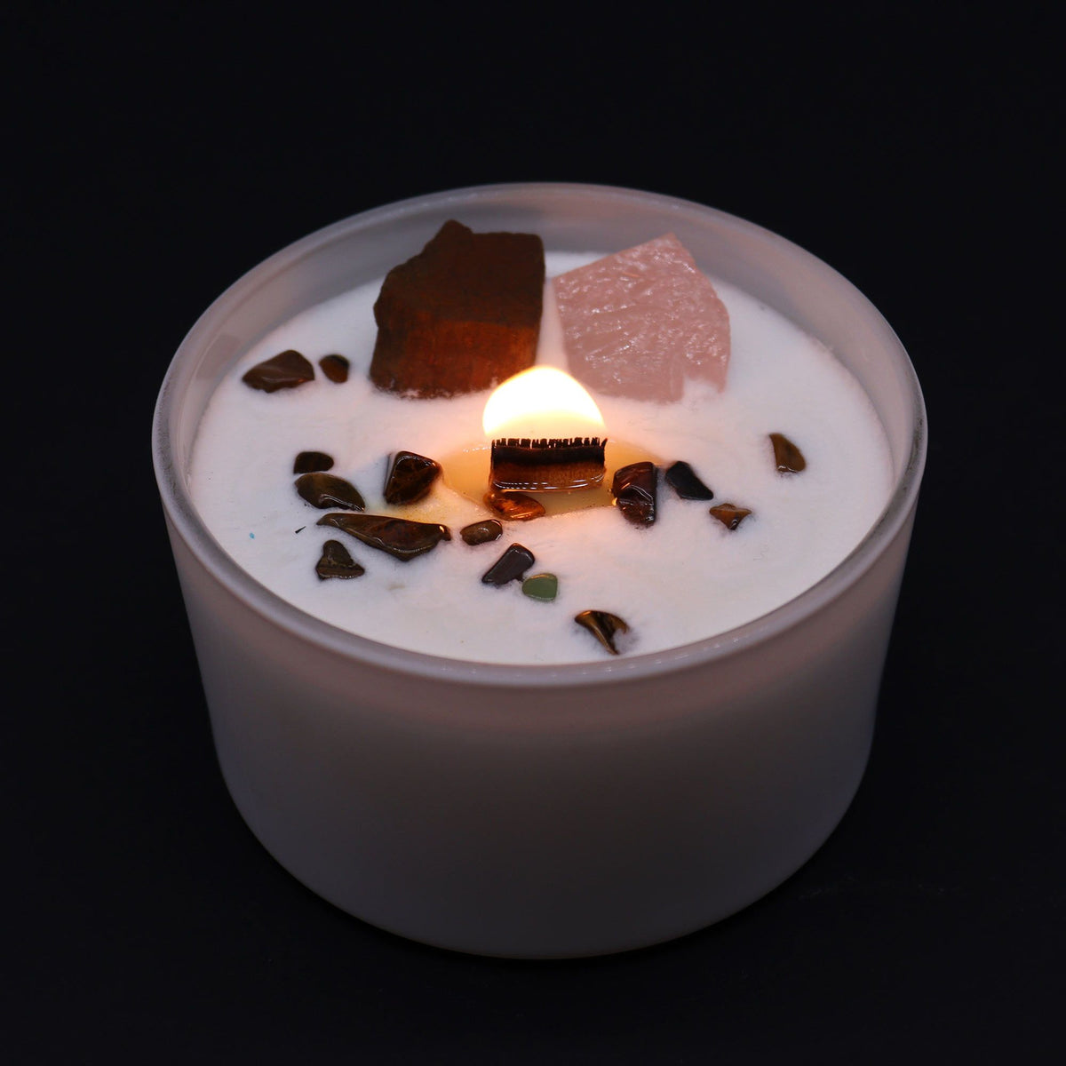 Lit white scented candle in a frosted glass jar with crystals and gemstones on top