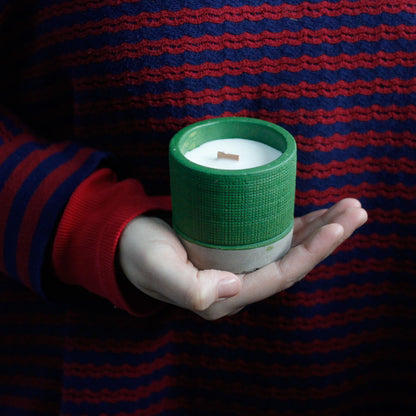 A person holding a small white candle in a green textured ceramic holder.