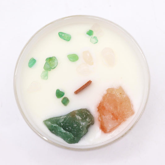 White scented candle with green and orange crystals and a small piece of wood.