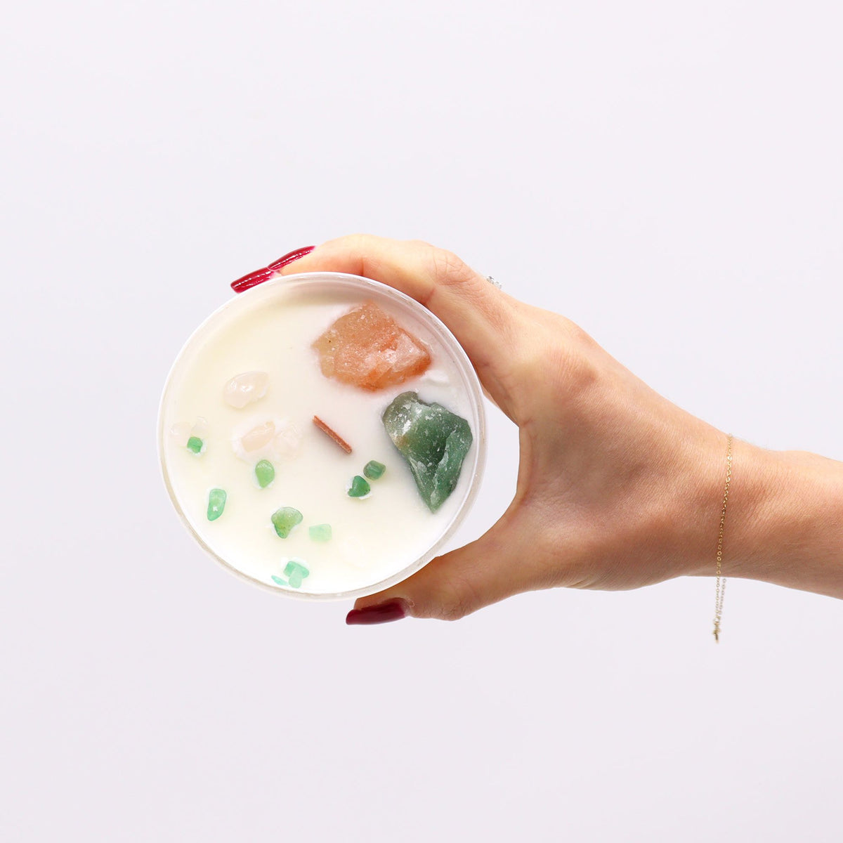 A hand holding a white candle topped with crystals and gemstones