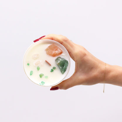 A hand holding a white candle topped with crystals and gemstones